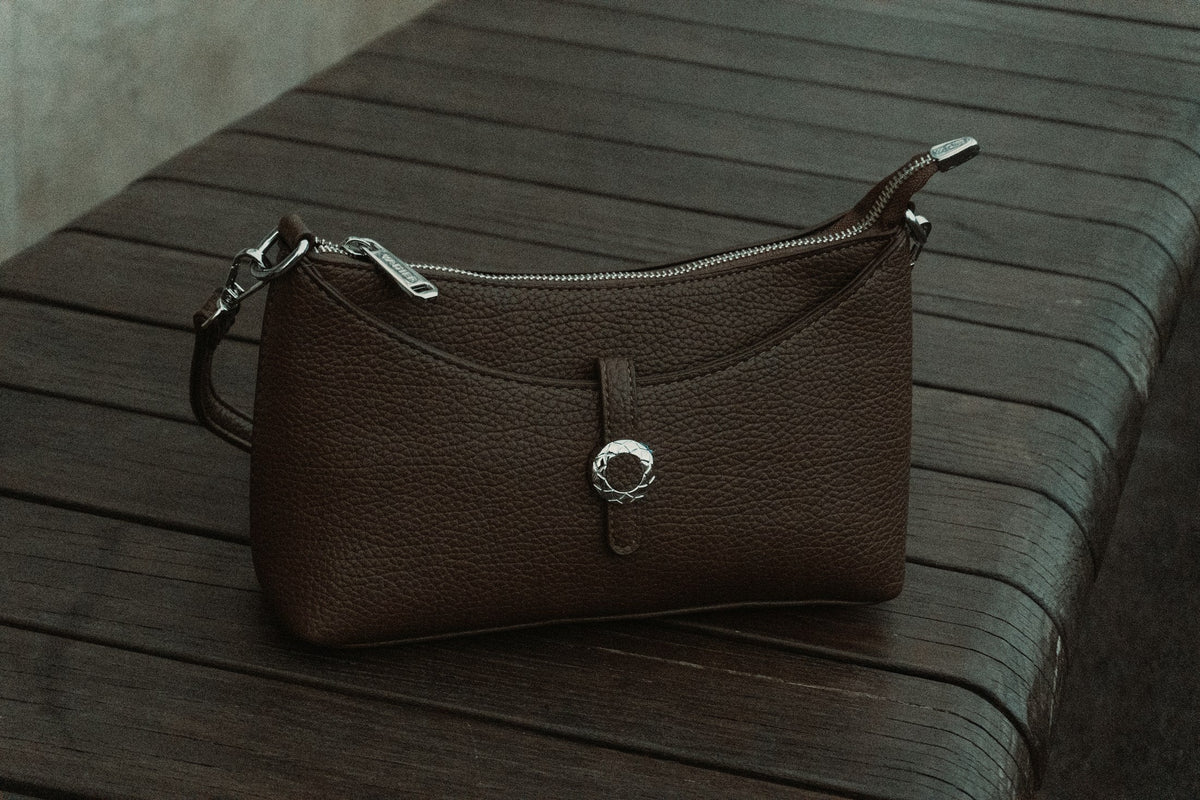Brown leather bag photographed on a dark timber surface, by Zulfugar Karimov